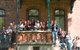 Das Foto ist ein Gruppenfoto vieler junger Menschen, die in die Kamera schauen und klatschen. Die Gruppe steht auf einer Art Balkon und Treppen, die links und rechts vom Balkon zum Boden führen. Der Balkon und das Gebäude, zu dem der Balkon gehört, sind aus Backstein. Über der Gruppe ist etwas versetzt ein zweiter Balkon mit Holzverkleidung. Im unteren Bildteil ist das Jubiläumslogo der SBB über das Bild gelegt, im oberen Bildteil steht über das Bild gelegt der Text "Geburtstagsgrüße Teil 3"