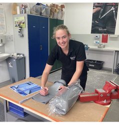Johanna Himmelberg steht an einem Arbeitstisch in der Werkstatt und zeichnet auf dem Werkstoff eine Schnitt-Linie.