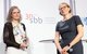 Antje da Silva Santos und Melanie Lochner stehen gemeinsam auf der Bühne. Frau Weiler steht links und hält den Preis in der Hand.